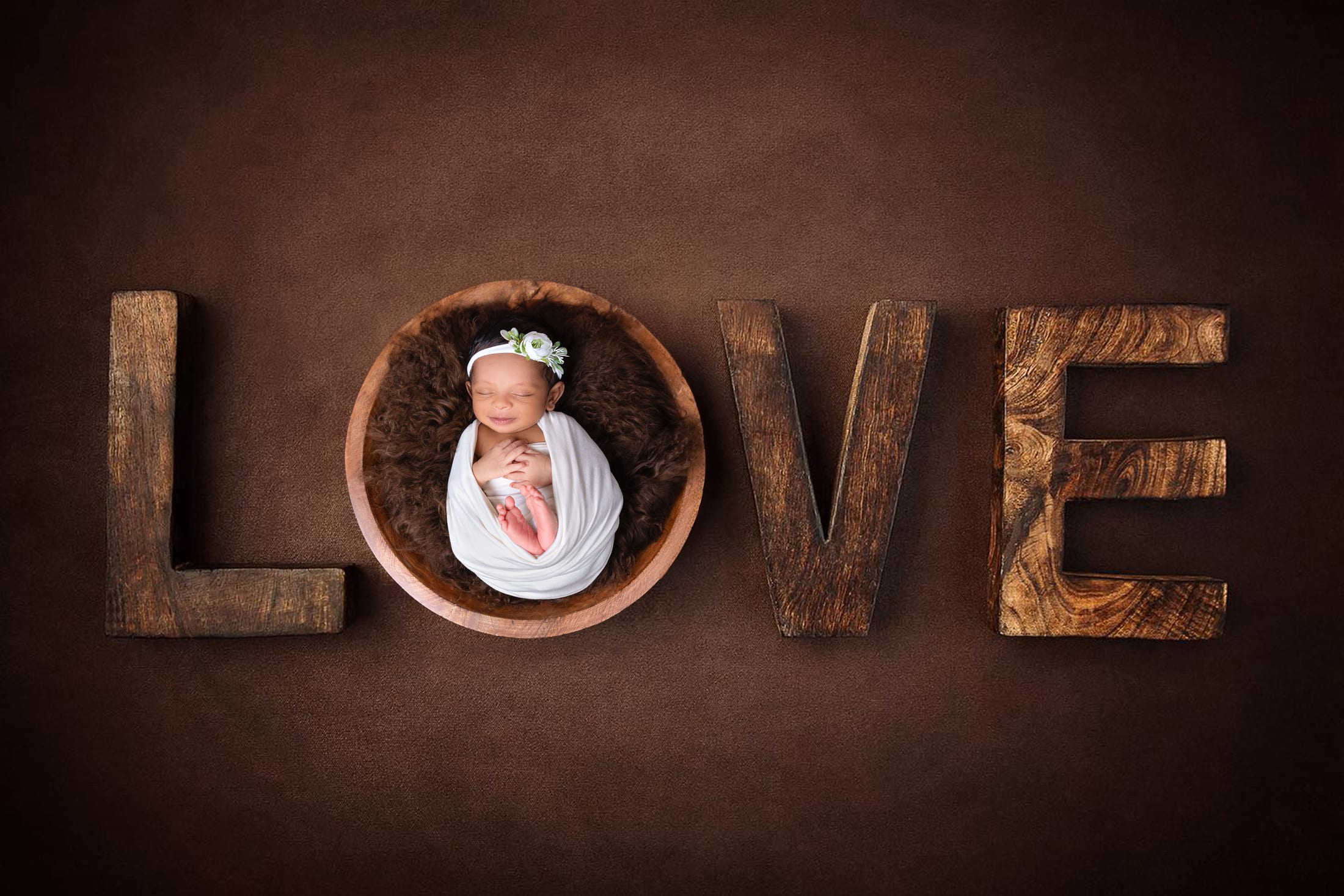 Newborn curled in a wooden bowl beside LOVE letters