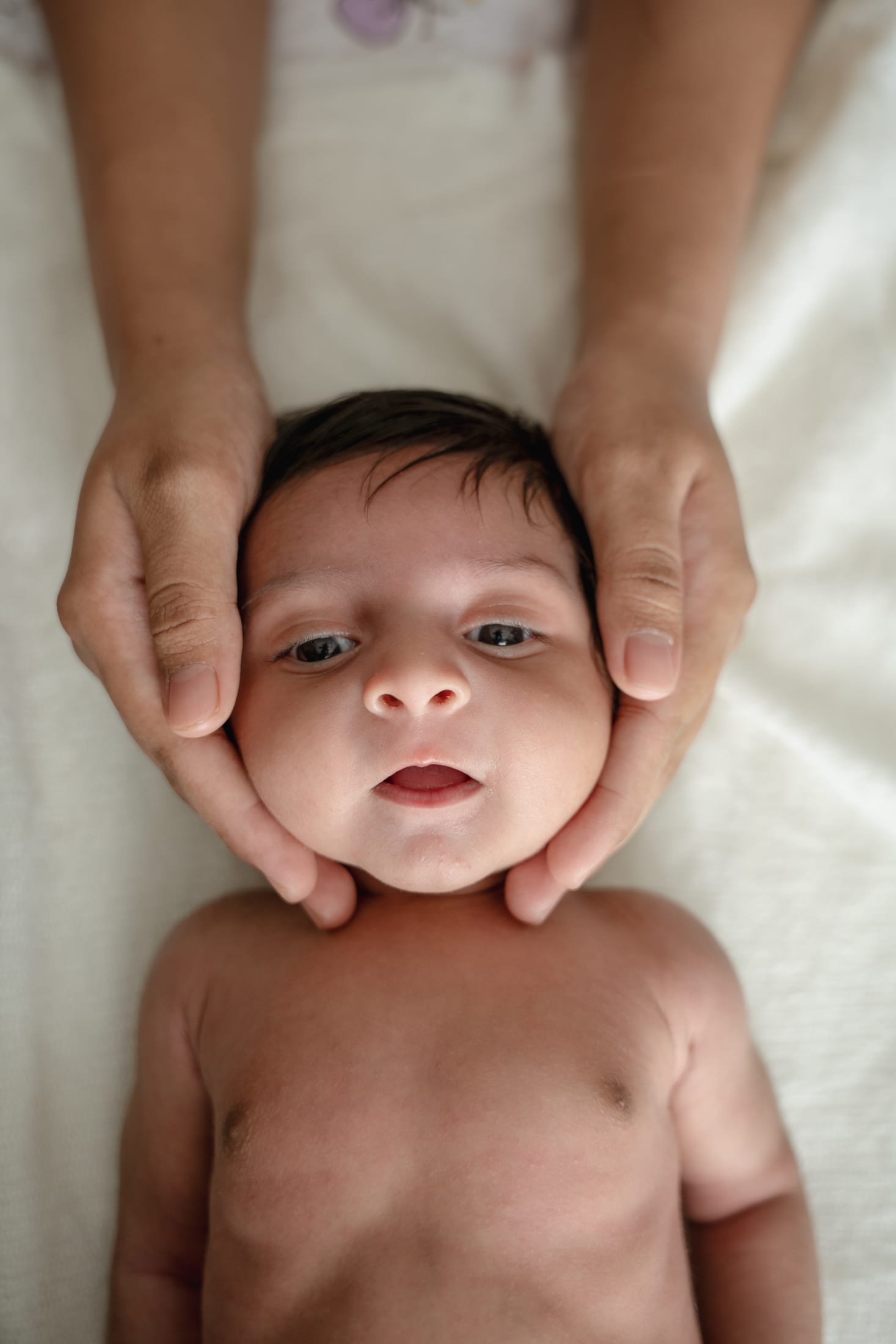 Parents' hands gently cupping their newborn's face
